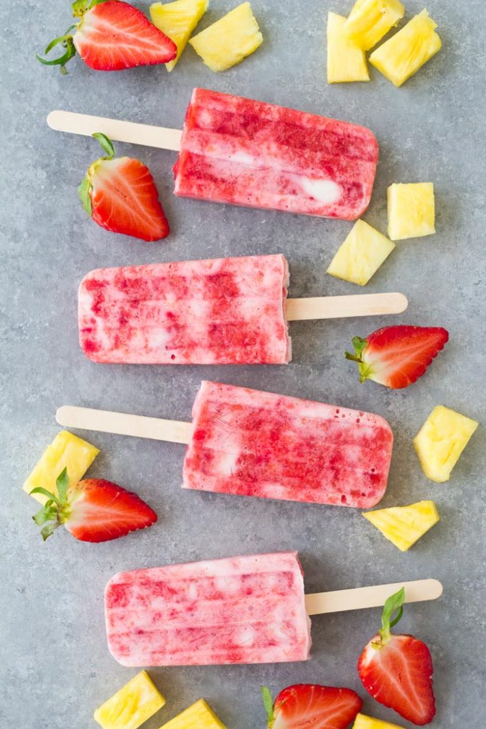 These Fruit and Yogurt Popsicles are easy to make and bursting with fresh fruit flavor! This homemade strawberry popsicle recipe is made with only four ingredients. These healthy popsicles are a fun summer treat for kids! Fruit and yogurt popsicles with strawberry and pineapple.