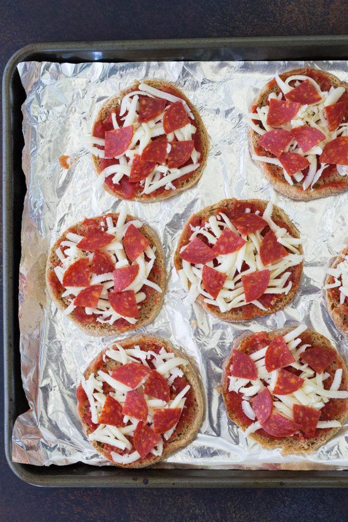These English Muffin Pizzas are perfect for kids! These pizzas are made in the oven and they are almost the same as regular pizza, but easier! The best easy mini pizza recipe, with lots of ideas for toppings including pepperoni or healthy veggies. Perfect for kids lunches, snacks or dinner! English muffin pizzas with cheese and pepperoni, before baking.