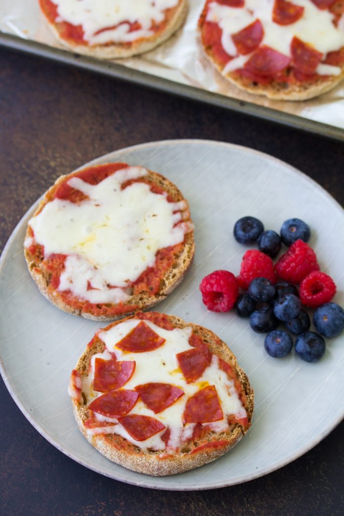 These English Muffin Pizzas are perfect for kids! These pizzas are made in the oven and they are almost the same as regular pizza, but easier! The best easy mini pizza recipe, with lots of ideas for toppings including pepperoni or healthy veggies. Perfect for kids lunches, snacks or dinner! English muffin pizzas on a plate, served with berries.