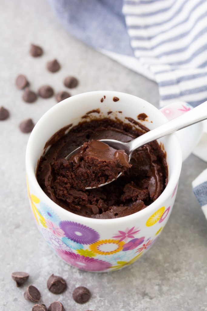 An easy chocolate mug cake that tastes like a brownie in a cup. This chocolate cake in a mug is a delicious microwave dessert that even a kid can make! This recipe has no egg and cooks in just 1 minute! A bite of fudgy chocolate mug cake on a spoon.